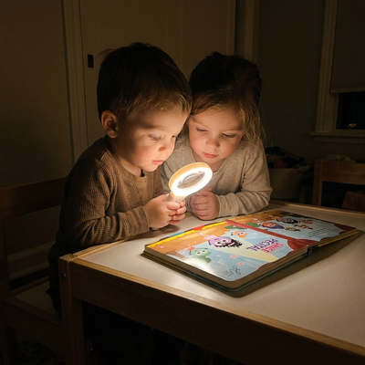 Two young siblings at a low table sharing the glowing Magic Magnifier over Lumi's First Dance Recital